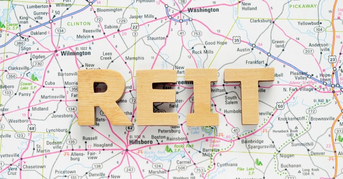 How to invest in REITs. Wood letters spelling out REIT on road map